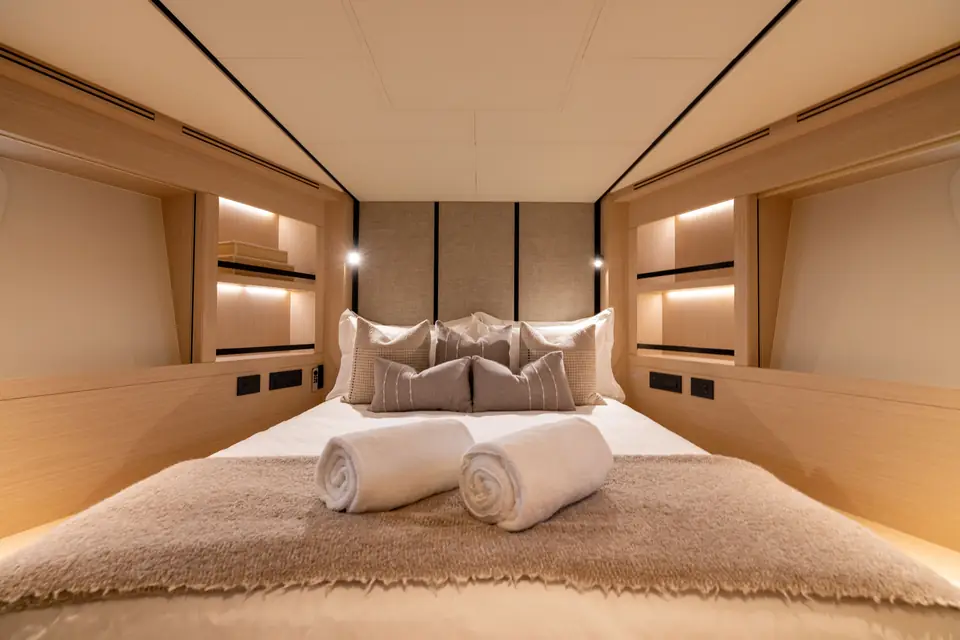 A guest cabin: berth against the hull side, reading light recessed, hull window at pillow height.